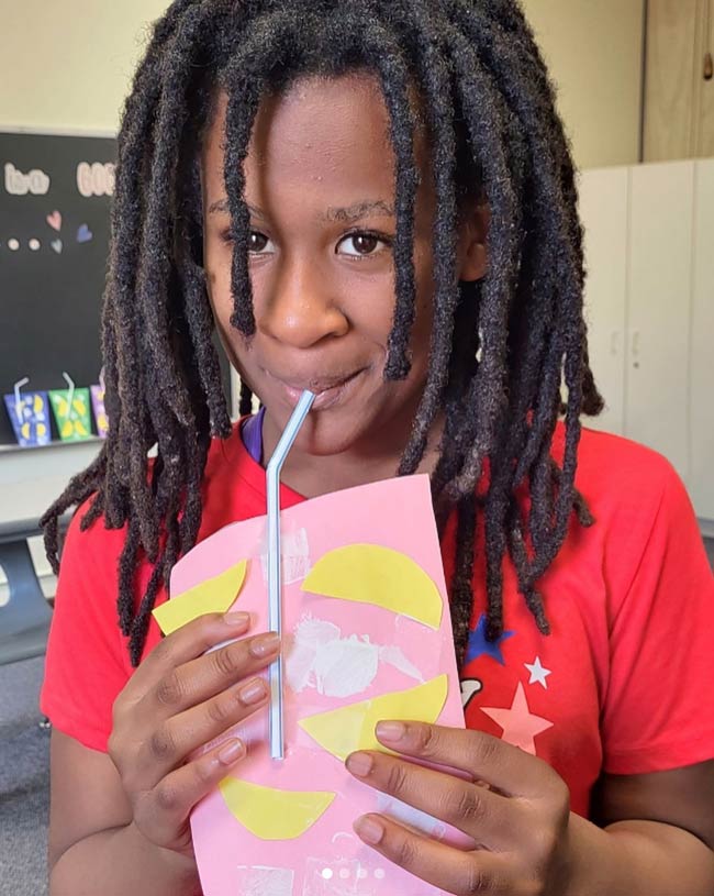 Smiling girl holding artwork with a straw.