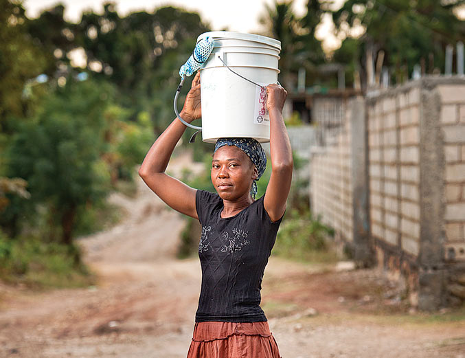 A Haitian woman carries a bucket of water on her head.