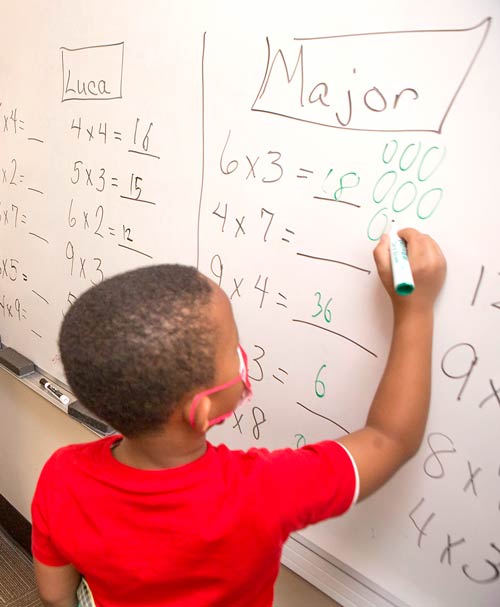 Boy student doing math at a whiteboard.
